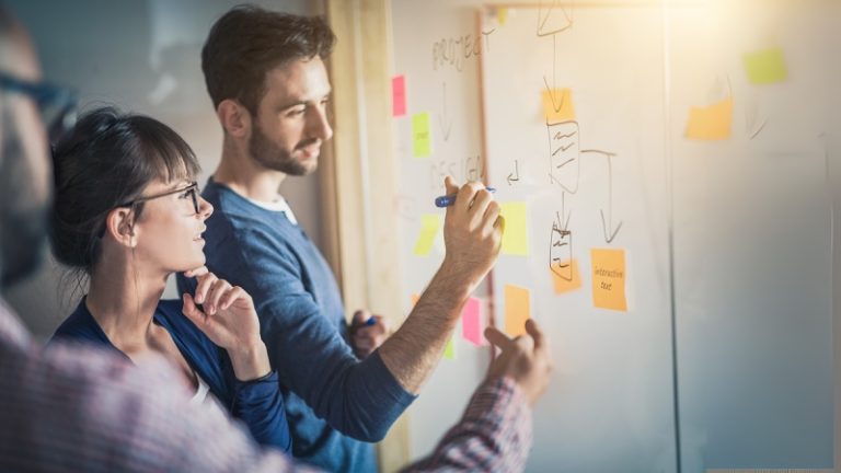 Trois personnes devant un paperboard pendant une formation, en pleine réflexion sur un sujet.